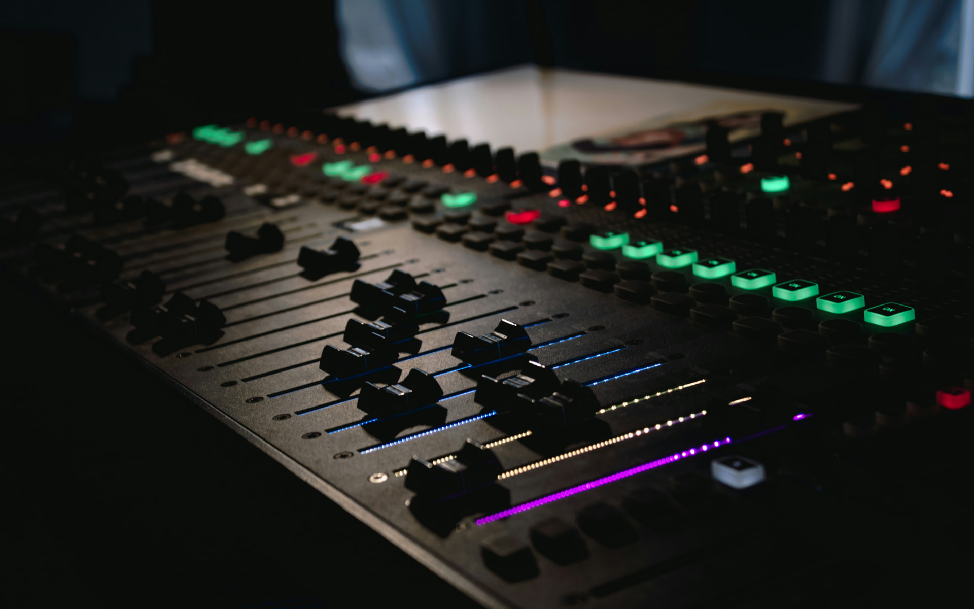 Professional audio mixing console with illuminated faders in a dim studio